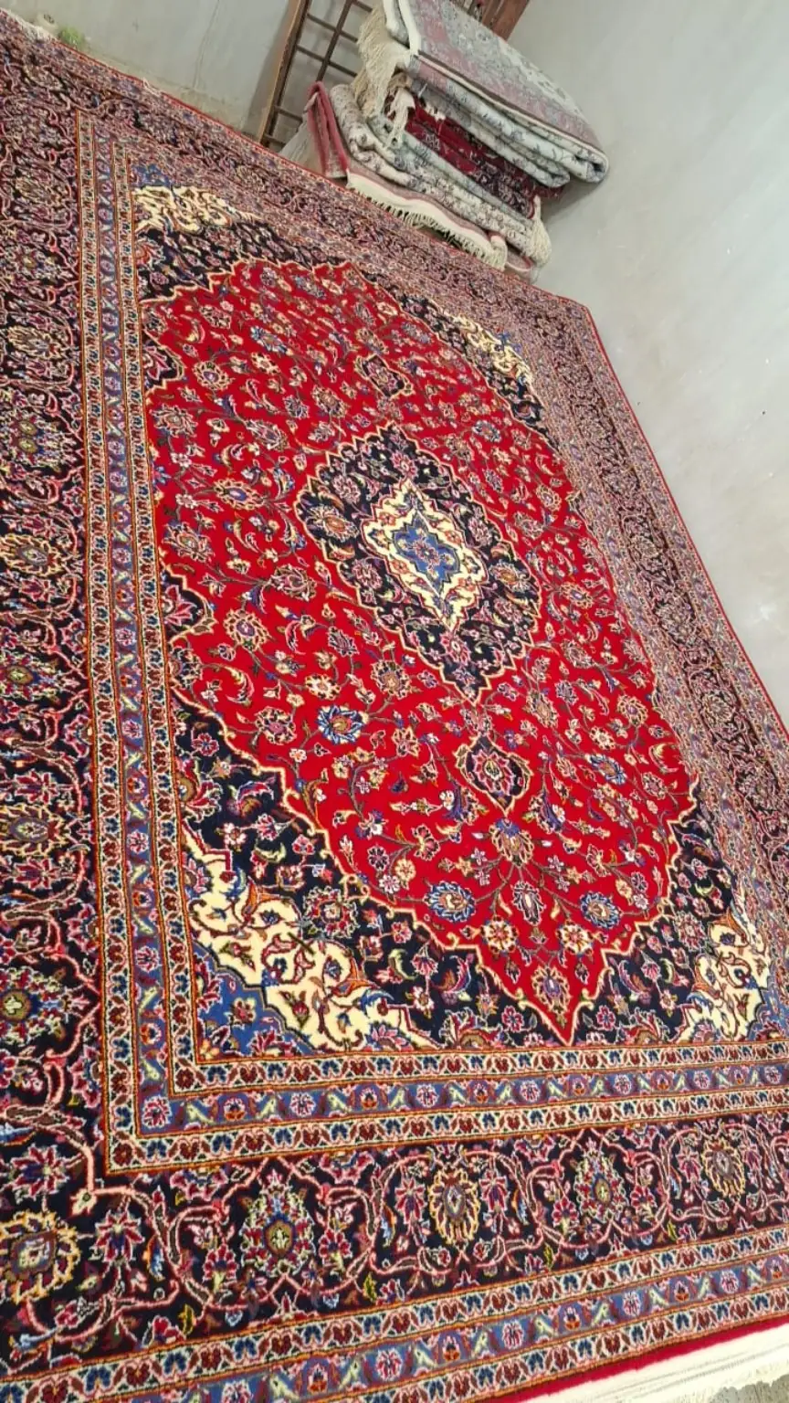 Angled full view of Royal Herati Medallion handmade Kashan carpet PRR-KH-029 with red field and navy medallion